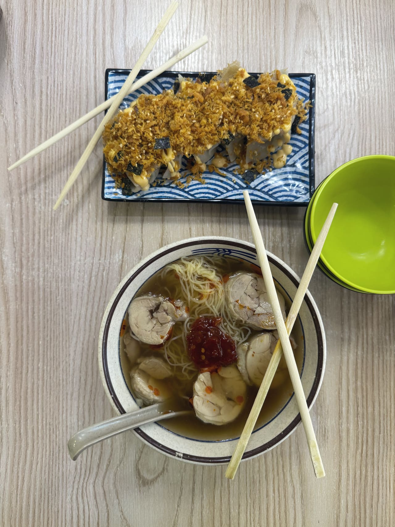 A plate of dumplings buried under fried garlic, sesame and crumbled seaweed, beside a bowl of thin noodles with poached rolls and a spoon of chilli