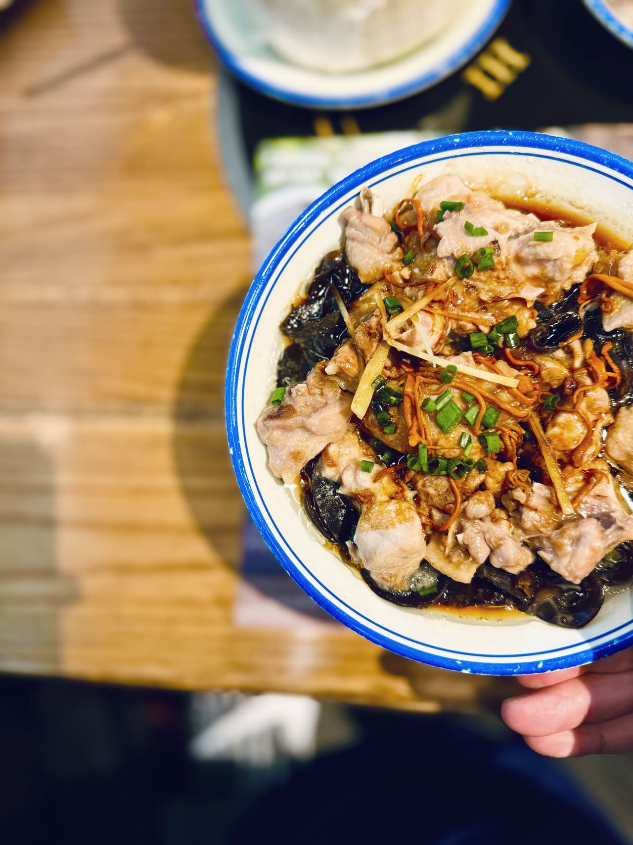 A bowl held over the table: steamed chicken with wood ear mushrooms, ginger and spring onion, rice waiting behind it