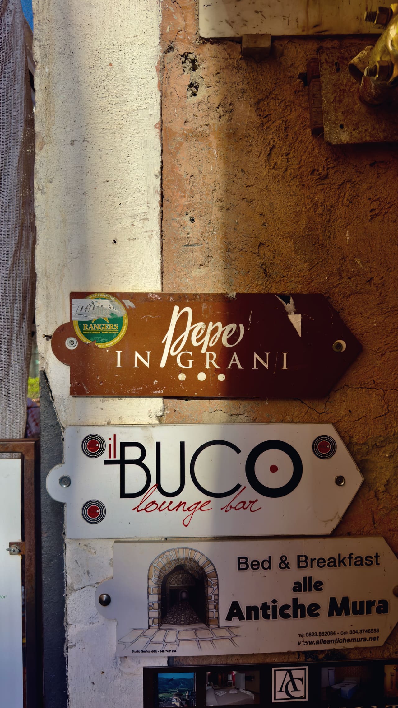 Three enamel signs screwed to a rendered wall, the top one pointing the way to Pepe in Grani
