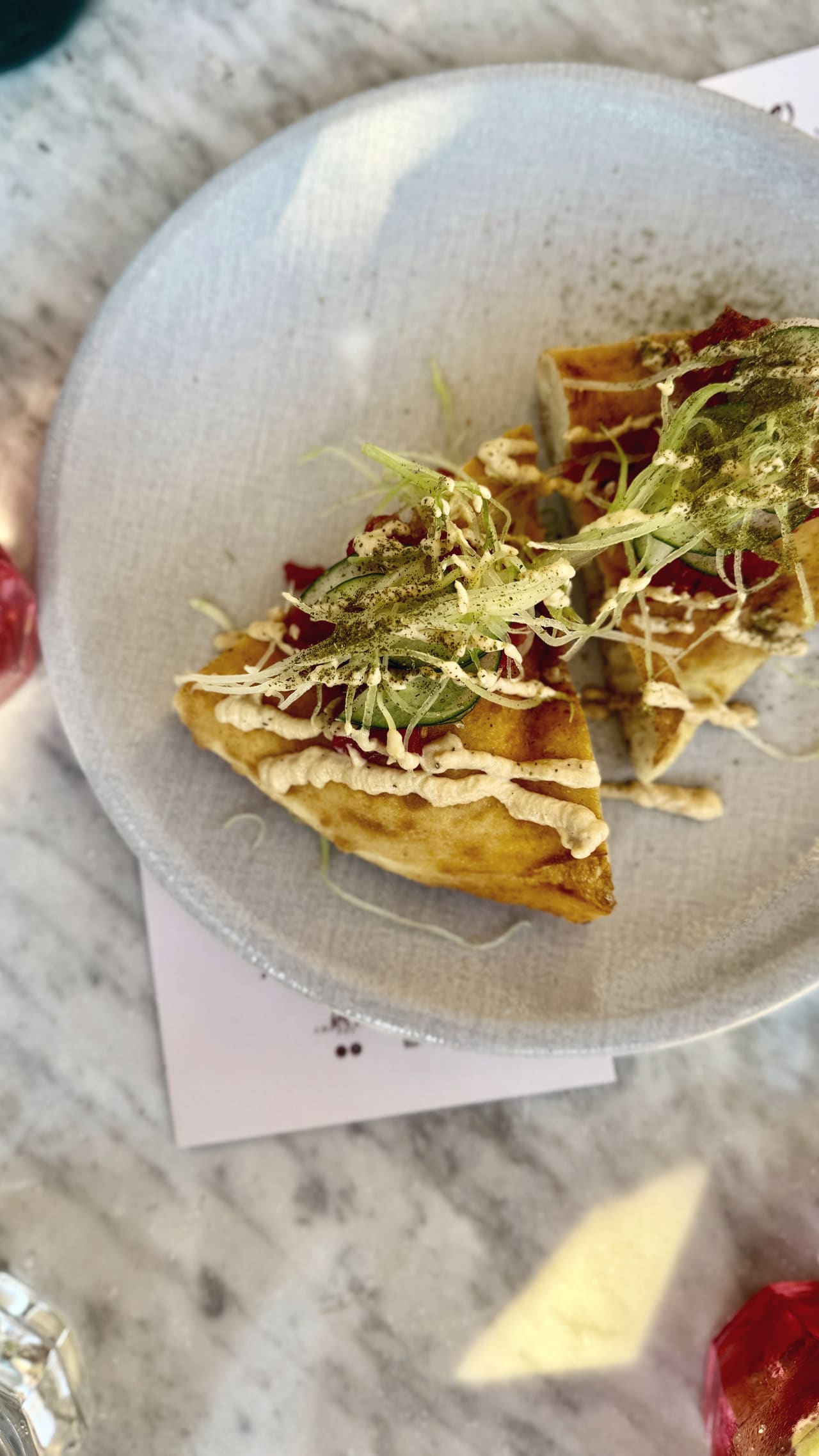 Two wedges of fried pizza on a stoneware plate, piped cream, cucumber slices and shredded fennel over the top