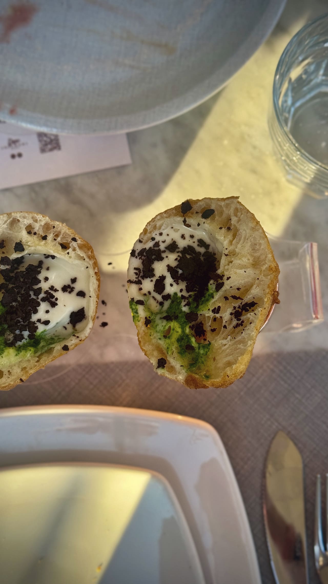 Two halves of a puffed fried roll opened out, filled with white cream and green herb sauce, scattered with dark crumb