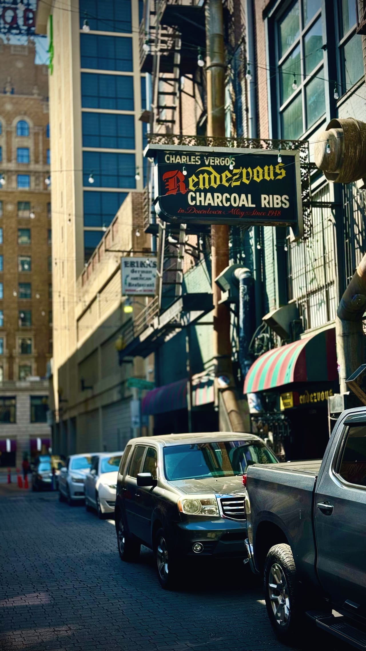A painted iron sign hung over an alley: Charles Vergos’ Rendezvous, charcoal ribs, in a downtown alley since 1948