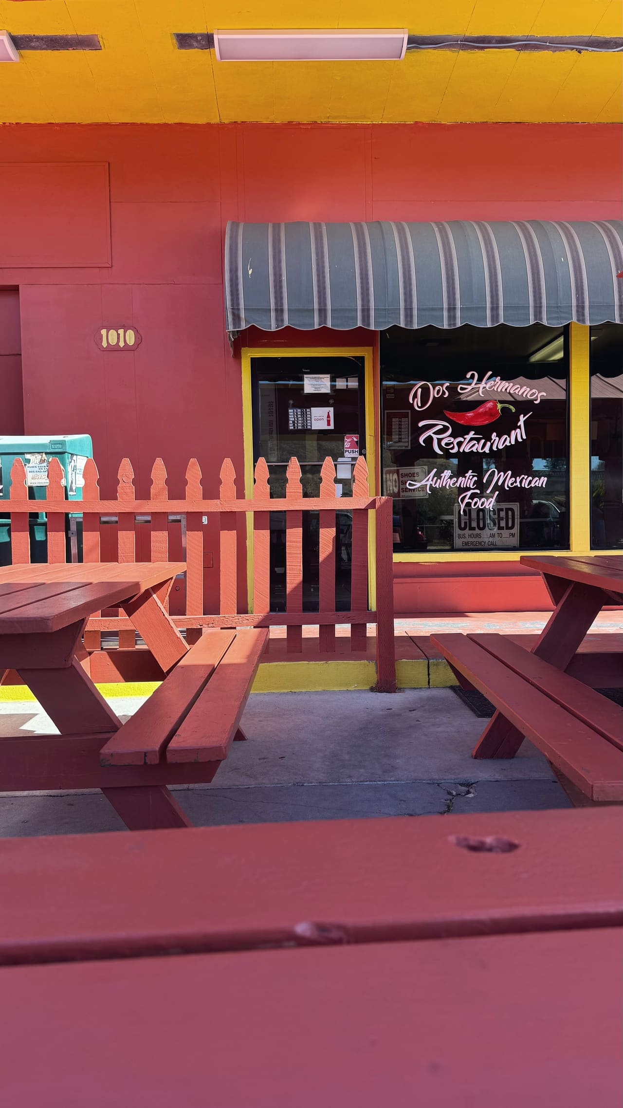 A closed Mexican restaurant painted red and yellow, empty picnic tables on the pavement outside
